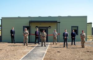 8 men standing in front of a newly built accommodation building smiling at the camera. Some dressed in military uniform, others in suits.
