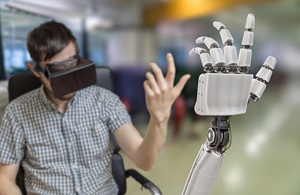 A man wearing a pair of virtual reality glasses lifting his arm up to show a robotic arm underneath.