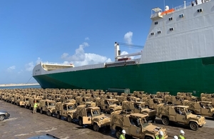 Dozens of armoured vehicles are lined up next to a cargo ship after being unloaded in a port.