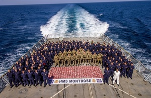 Dozens of Royal Marines and sailors stand around the confiscated 2.4 tonnes of drugs in red bags on the deck of HMS Montrose.