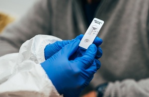 A lateral flow device test being held in someone's hand who is wearing surgical gloves