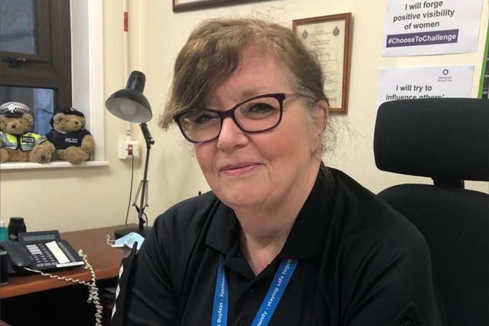 Fiona sits at her desk. There are bears on a window sill and an International Women’s Day poster behind her.