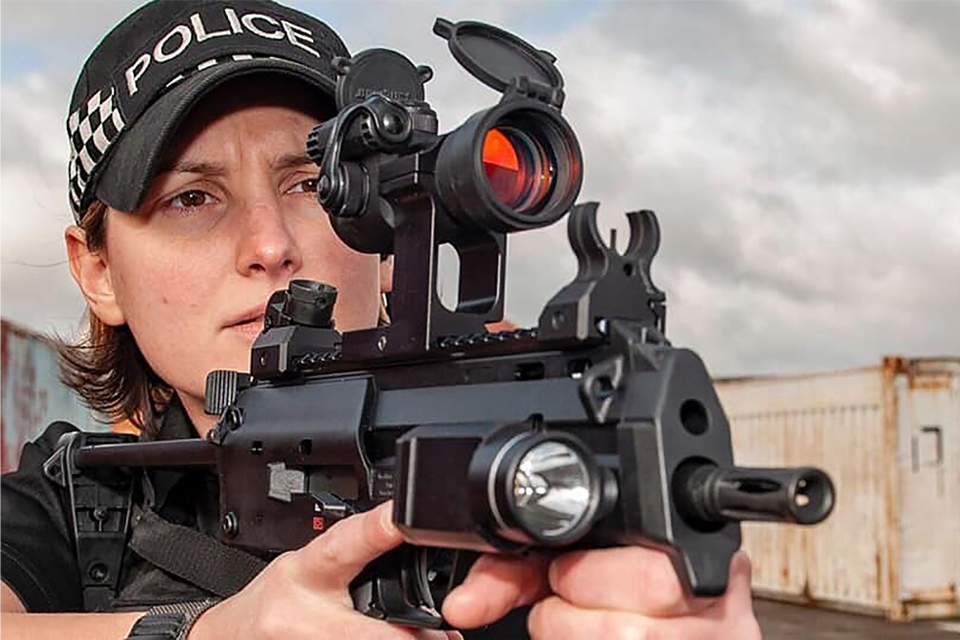 Sally looks through the eyepiece of her firearm. She wears MDP uniform.