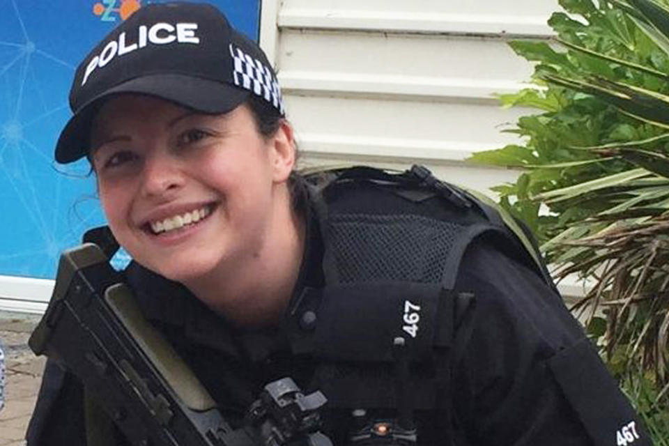 Nicole is seated smiling in her poiice uniform. She holds a firearm.