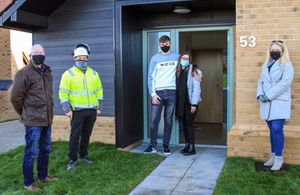 The photo shows a young man and woman being welcomed to their new home by a property developer and two members of the local Community Land Trust.