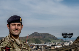 Pictured on the left hand side of the image in uniform with buildings and landscape in view behind him.
