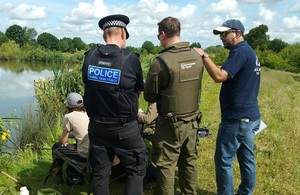 A police officer, Environment Agency officer and Angling Trust volunteer in uniform facing anglers at a riverbank.