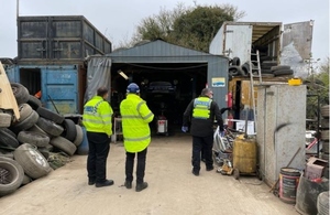 Image shows an Environment Agency officer with two British Transport Police officers all wearing high visibility jackets, inspecting a garage surrounded by old wheels and tyres