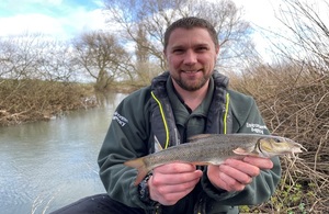 A fisheries officer holding a barbel fish along the River Ouse at Ravenstone Mill.
