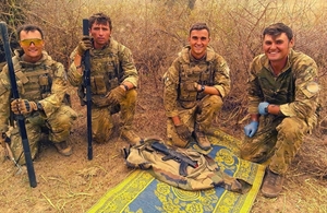 British peackeepers smile as they kneel and pose next to one of the AK47 rifles found.