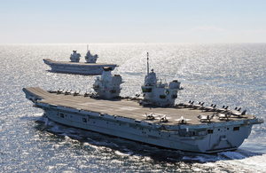 HMS Queen Elizabeth and HMS Prince of Wales, two Royal Navy aircraft carriers, are shown at sea with the sun shining brightly