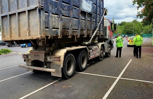 Image shows large container lorry in a car park to the left with police and Environment Agency in high visibility jackets to the right