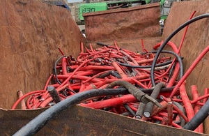 Image shows rusty skip full of lengths of thick red cabling and pieces of black cabling