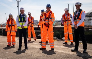 Image shows 7 people wearing high visibility clothing and hard hats standing by a quayside