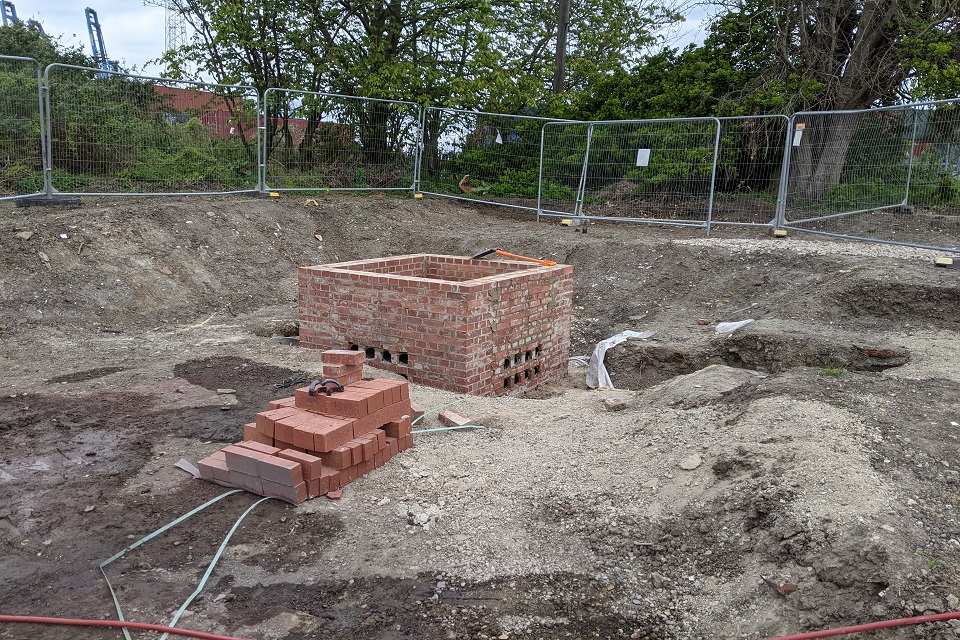 Image shows four walled, open top brick structure in centre of a wide earthen pit