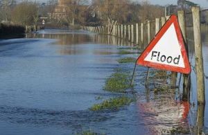 A flooded road in the countryside with a flood sign
