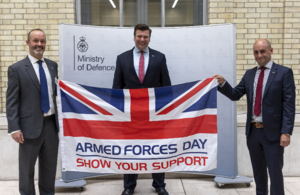 John Boumphrey, VP Country Manager UK for Amazon and Chris Hayman, UK Public Sector General Manager at Amazon Web Services hold a flag which reads Armed Forces Day, Show Your Support. Minister for the Armed Forces, James Heappey stands in between them.