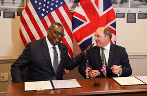 Ben Wallace and Lloyd Austin laugh as they sign the extension in front of UK and US flags
