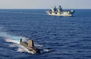 An Astute Class Submarine on the surface with UK aircraft carrier HMS Queen Elizabeth in the background