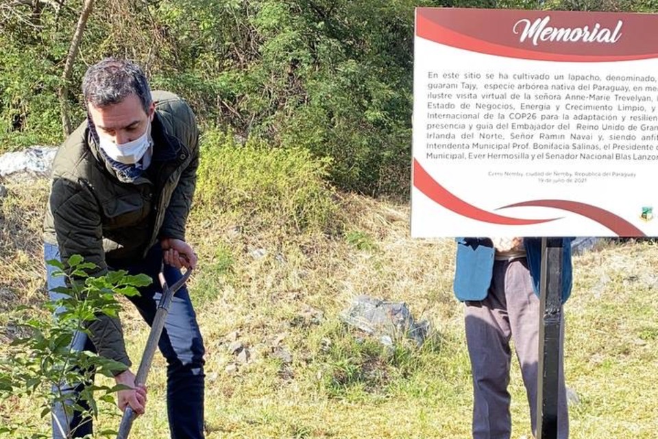 HMA Navai using a spade to plant a tree, standing by the memorial sign that commemorates the occasion