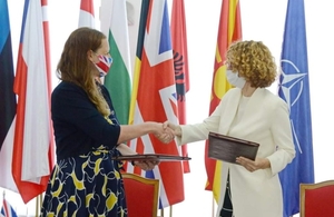 UK Ambassador Rachel Galloway and the Defence Minister for North Macedonia Radmila Shekerinska shake hands in front of the flags of NATO nations after signing the agreement