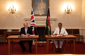 Ben Wallace and Dr Monica Juma sign the agreement in front of the Kenyan and UK flags