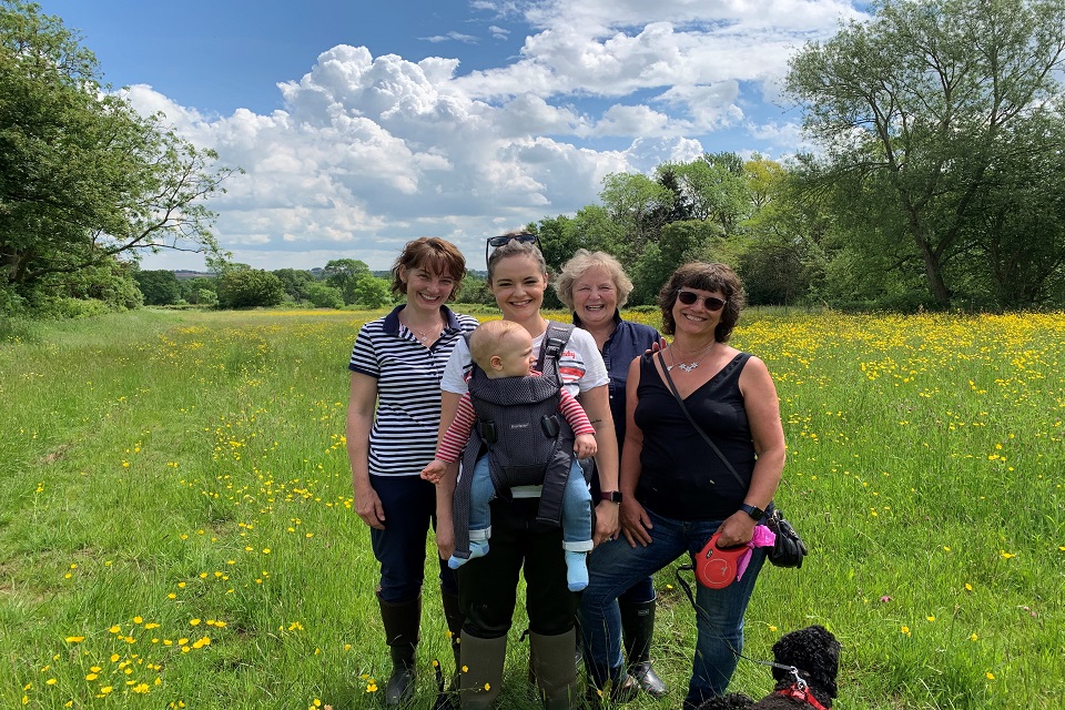 Image shows four female members of the Johnson family, plus a baby and a small black dog, in a field of tall grass and wildflowers