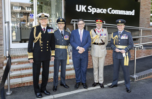 Министр оборонных закупок Джереми Куин и военное руководство улыбаются, стоя вместе перед новым космическим командованием Великобритании.