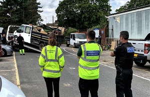 Image shows white pick up truck carrying waste being loaded onto a recovery vehicle to the left of the picture, while staff from the Environment Agency, National Enforcement Service and the police look on