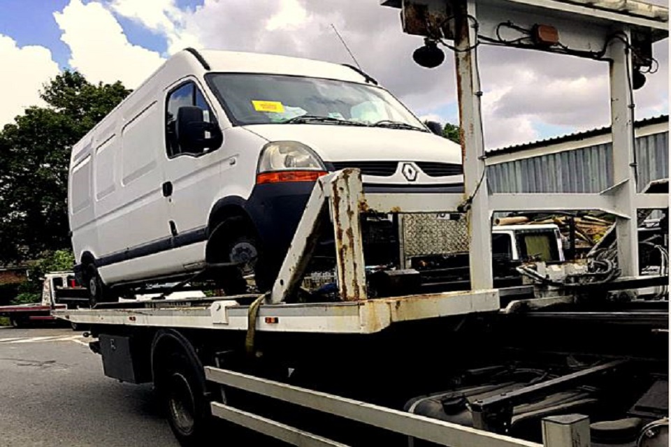 Image shows large white panel van loaded on the back of a transporter