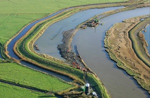 Image shows several river channels curving in concentric loops across green fields. There are barges with lifting equipment moored against one bank