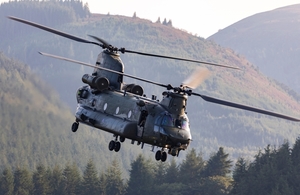 A Chinook helicopter flies through a wooded valley.