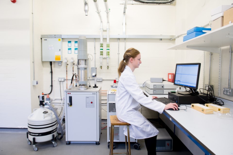 A researcher sits at a computer, surrounded by equipment