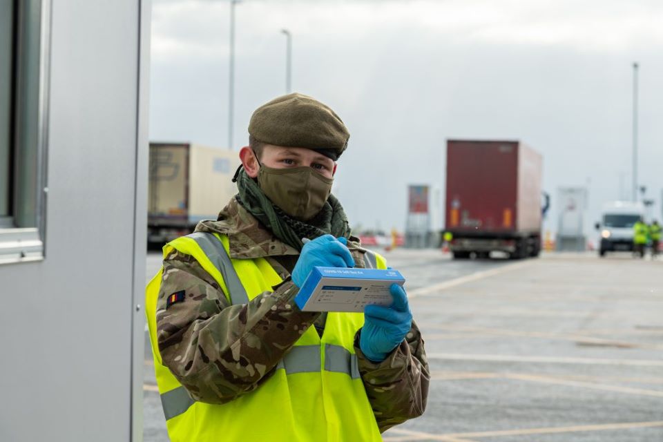 Private Ollie Wilson writes on a COVID-19 testing kit. He wears a face mask and camo uniform.