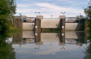 Image shows three gates located between four pillars stretching across a body of water. The middle gate is partially raised.