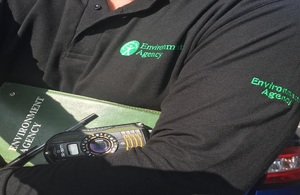 A close up of an Environment Agency officer's black sweatshirt and logo. The officer is holding a book.