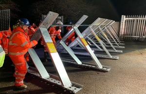 Image shows several people dressed in orange overalls assembling triangular sections of a flood barrier support