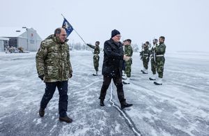 Министр обороны и его шведский коллега идут по взлетной полосе в аэропорту. Шведские солдаты стоят по стойке регистрации на заднем плане.