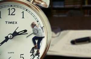 Woman climbing on clockface with background blurred image of notepad and pen on study desk