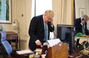 Борис Джонсон стоит за своим столом и разговаривает по телефону с президентом Украины Владимиром Зеленским.