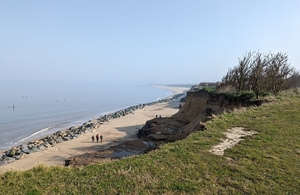 eroded cliff edge with beach and blue sky in background