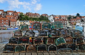 An orderly pile of lobster traps by the harbour. On the Background Whitby harbour.