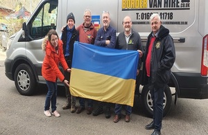 Группа мужчин и одна женщина стояли перед фургоном доставки. Они держат украинский флаг.