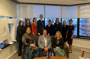 Sir Ian Botham sitting on a lounge in an office surrounded by the UK Government team in Brisbane.