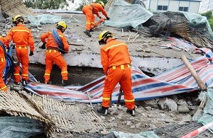Team of rescuers, wearing orange clothing and yellow hard-hat helmets, look for people in the rubble of a demolished building.