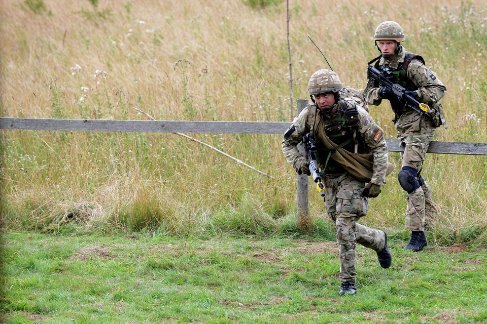 Soldiers cross a field whilst under fire