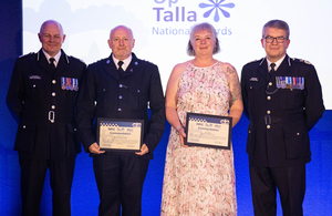 Three men and a woman standing in a line with ‘Op Talla National Awards’ sign in the background.