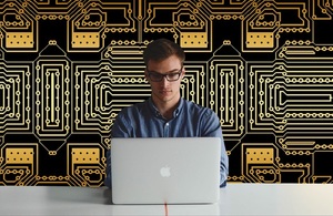Man working on computer with huge image of electronic circuits behind him.