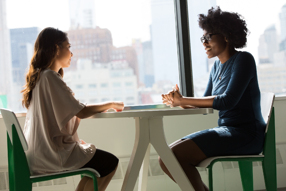 Two women sitting at a table close to windows overlooking city centre buildings