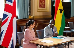 UK Home Secretary Priti Patel and the Minister for National Security of Ghana Kan-Dapaah seated at a desk between the UK and Ghanaian flags.